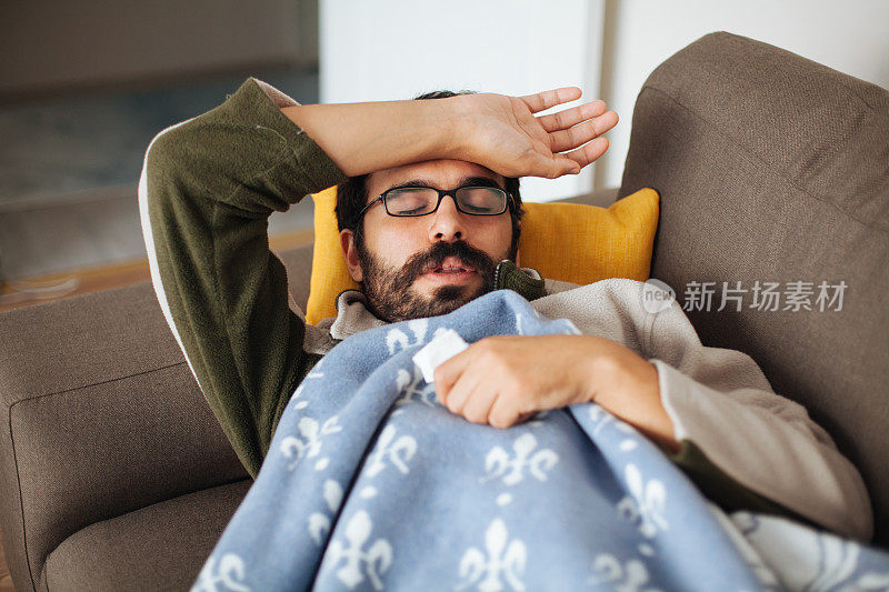一个感冒的男人拿着纸巾躺在沙发上