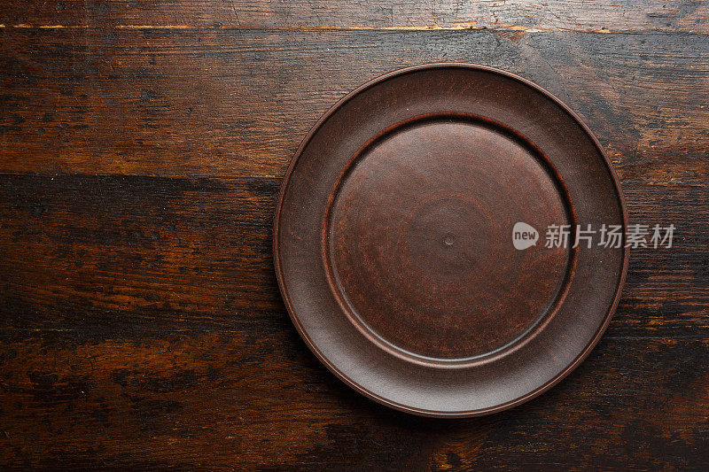 在棕色木制背景上的空的扁平粘土盘子
