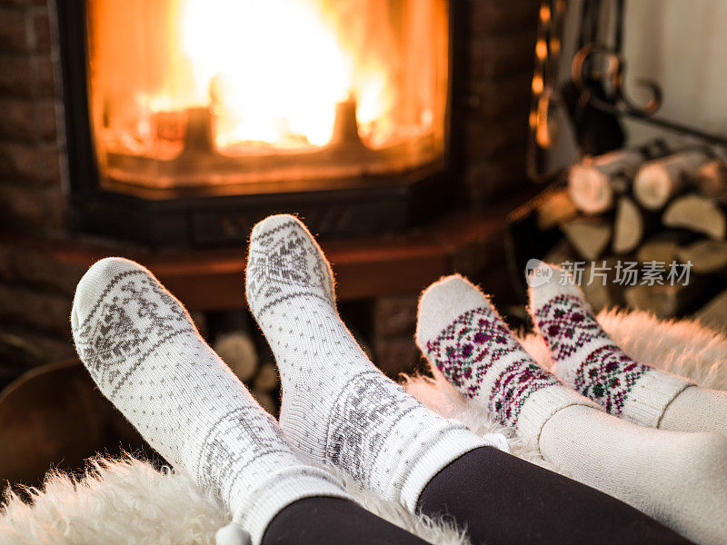 在壁炉旁取暖和放松。女人和小孩的脚在火前。