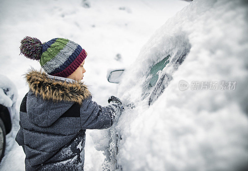 大雪过后，小男孩在清理汽车上的积雪