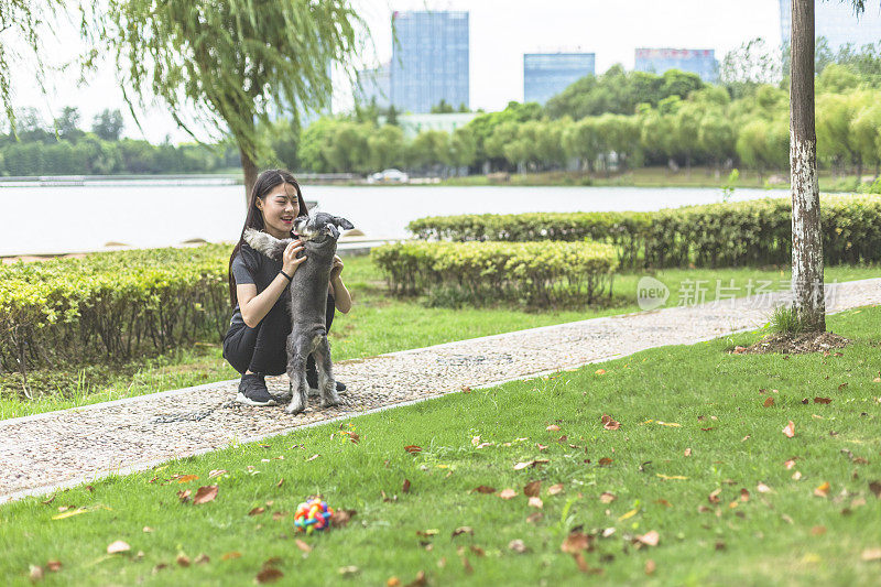 美丽的女主人和她的小狗雪纳瑞在公园里玩