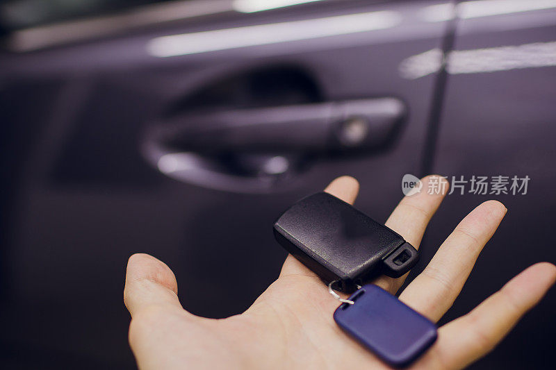 女人的手拿着车钥匙与黑色的汽车背景。