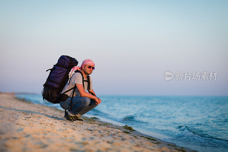 一个背包客蹲在海边