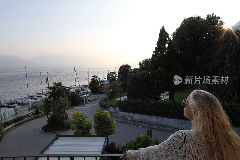 女人站在阳台门口，看着湖面上的日出