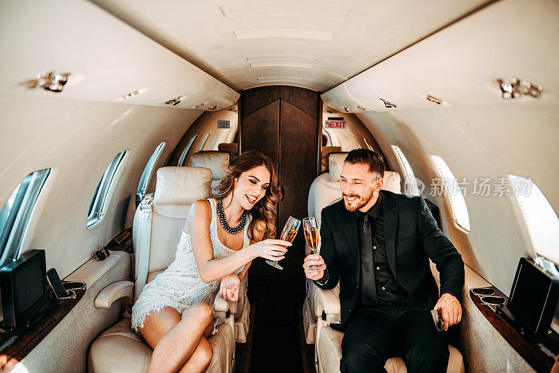 年轻富有，衣着考究的夫妇乘坐私人飞机旅行，喝香槟，敬酒。
