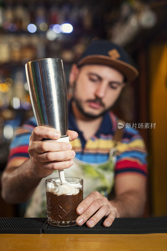 调酒师在玻璃杯中混合鸡尾酒，在上面倒入奶油