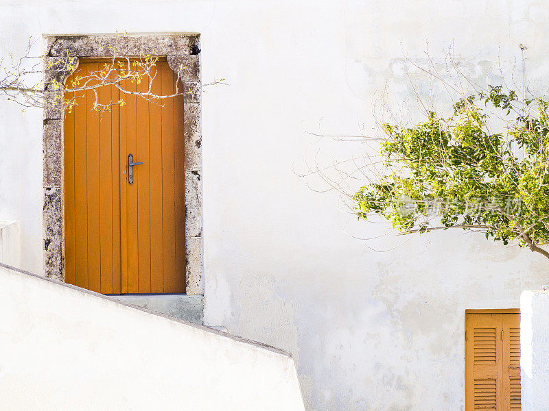 希腊圣托里尼岛，橘黄色的门，白色的墙和树
