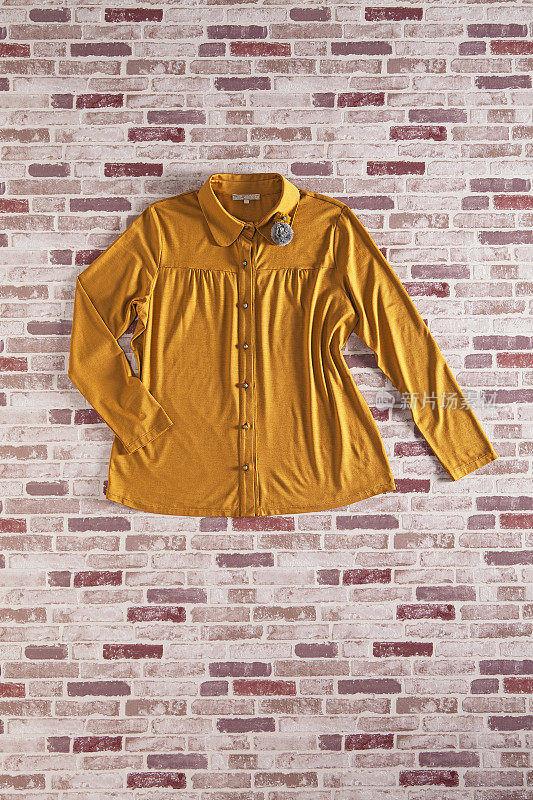 时髦的黄色衬衫孤立在砖背景上