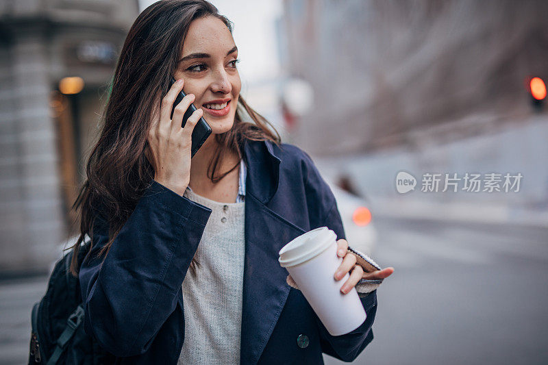 年轻女子在街上打电话，手里拿着一杯咖啡