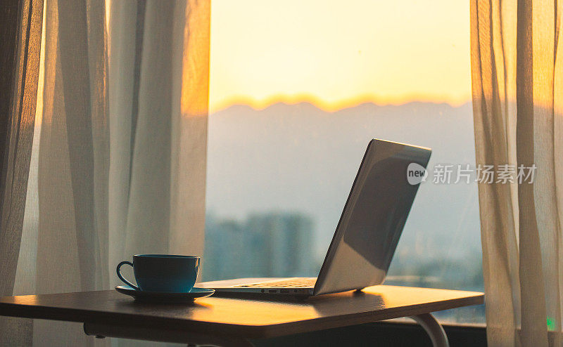 书桌上放着笔记本电脑，窗外是夕阳