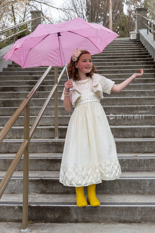 户外楼梯上带着亮色雨伞和靴子的可爱女孩