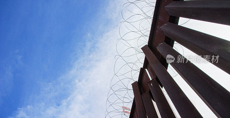 在墨西哥和美国之间的钢条边境墙(美国一侧)上的铁丝网在阴天