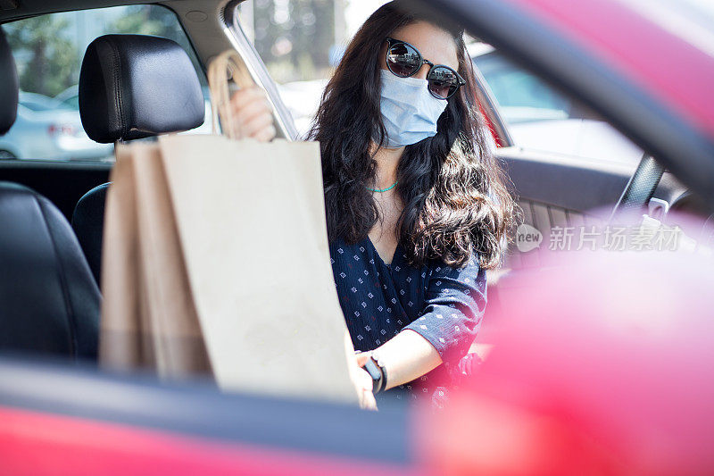 戴口罩的女人把购物袋放进车里