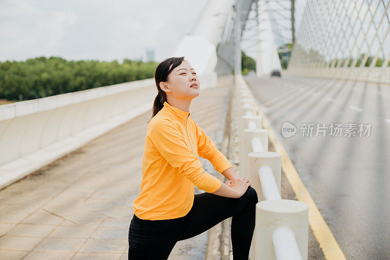 运动的亚洲华人妇女伸展她的腿和做热身运动在一座桥上