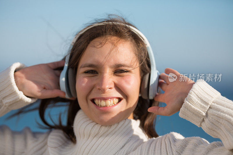 迷人的年轻女子在海滩上随着耳机里的音乐跳舞