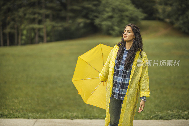 女人穿着雨衣，撑着雨伞，在雨天行走