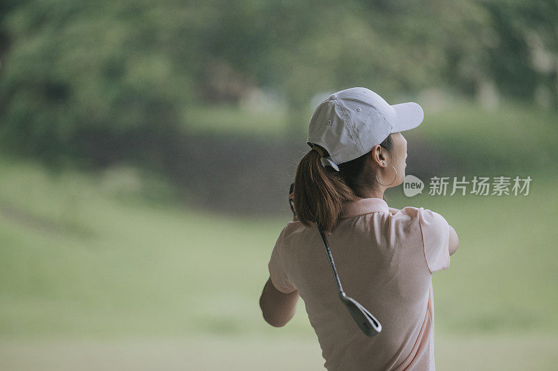 亚裔华人年轻女子高尔夫球在雨中挥杆高尔夫练习场