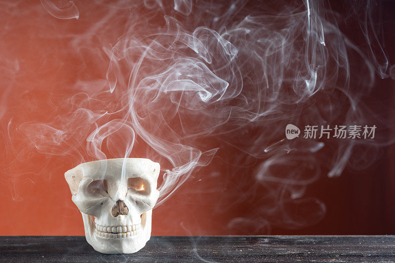 烟雾和人类头骨在橙色背景前的万圣节照片
