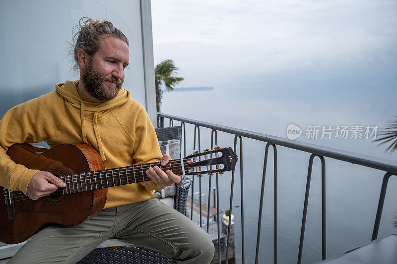 一个男人在自家阳台上弹吉他，可以看到湖景