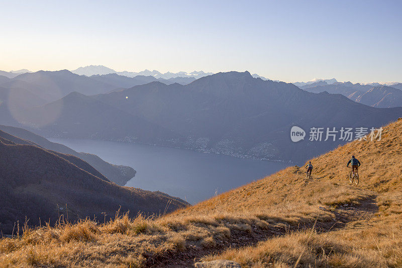 骑山地车的人在日出时从长满草的山脊上骑下来