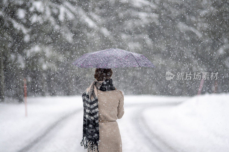 一个女人从后面打着伞下了雪