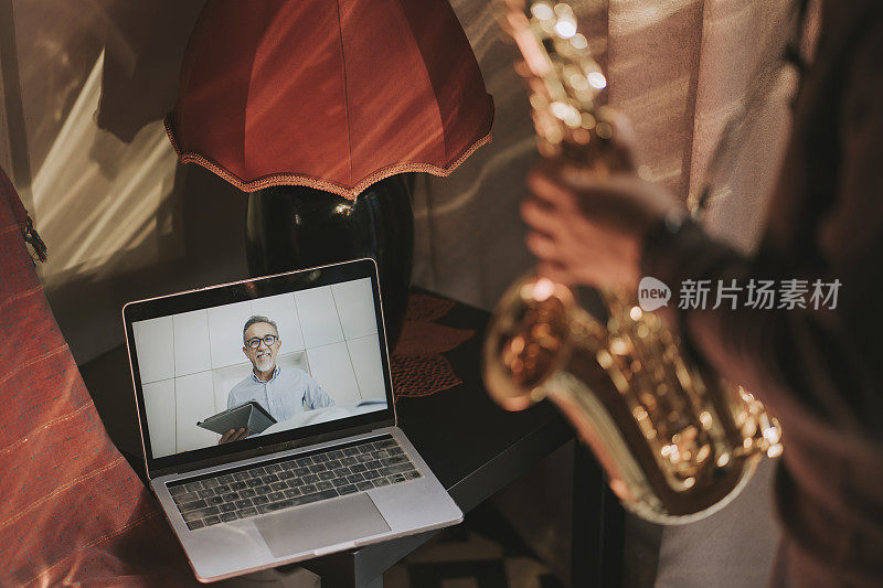 生活黑客亚洲中国中年男子练习萨克斯管在客厅的网上虚拟课堂上与他的导师使用笔记本电脑