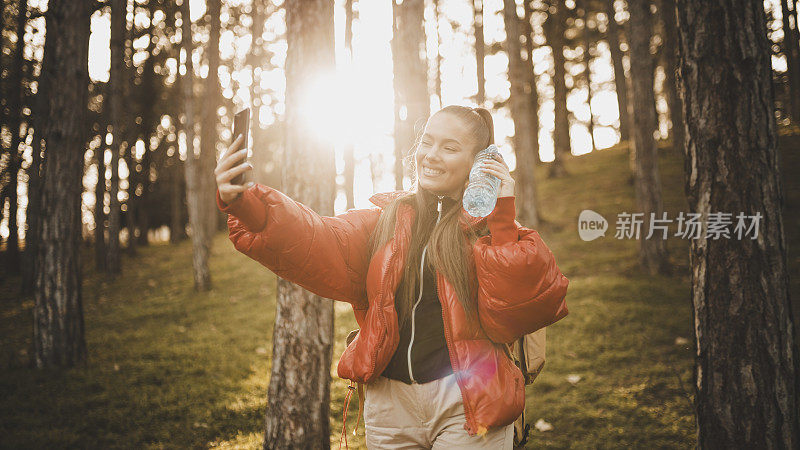 女人徒步旅行者用她的智能手机自拍和徒步在日出的山峰