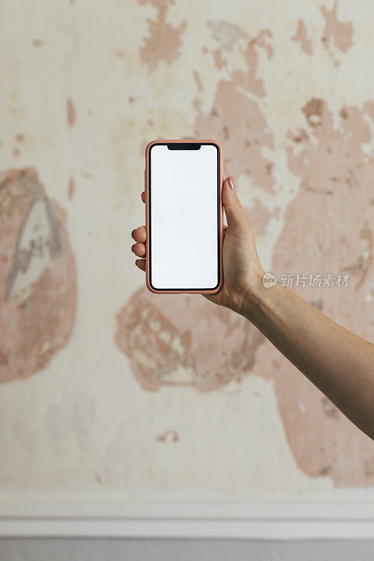 一个白人女人的手拿着一部智能手机，在墙上有一个复制空间触摸屏