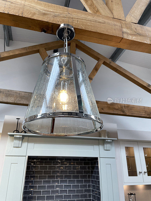 玻璃和铬合金的图像，悬挂的灯罩用链子挂在木头上，家庭房间的天花板横梁，照明灯泡，从下面看