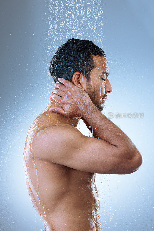 工作室拍摄了一个英俊的年轻人在淋浴中洗头发，背景是灰色的