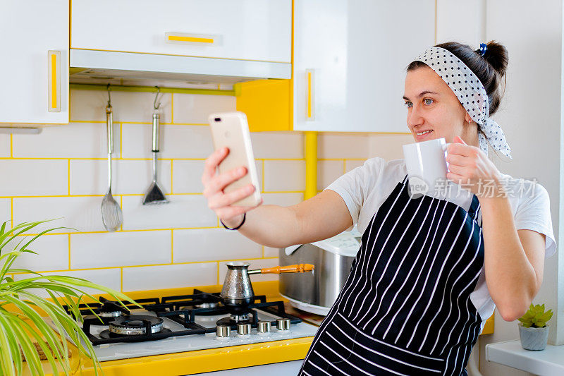 一名女子正在用智能手机进行视频通话。在厨房通过视频电话喝咖啡。概念远程通信，隔离