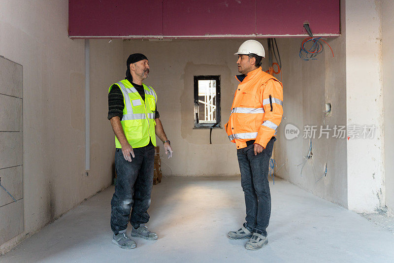工程师和工头穿着安全背心和安全帽交谈。