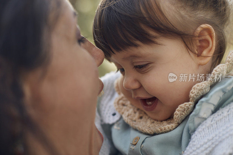 可爱的小女孩喜欢在公园里她妈妈的腿上玩。