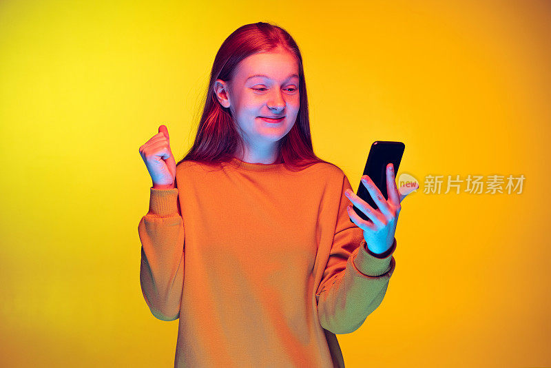 年轻兴奋的女孩有在线视频电话在黄色工作室背景霓虹灯孤立的肖像