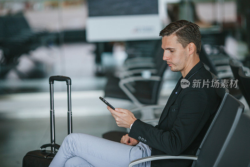 在机场候机室等待飞机的乘客。年轻人拿着智能手机在机场候机