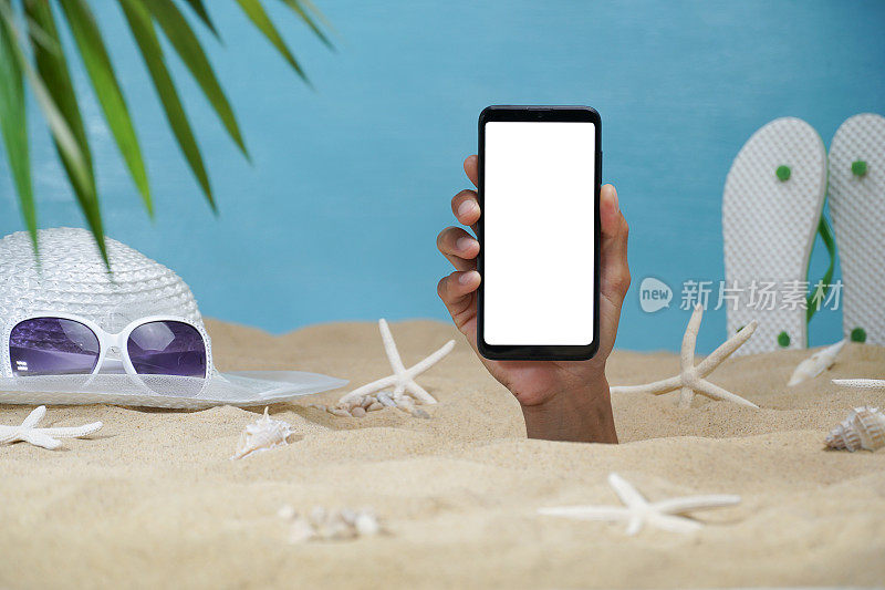 手拿着白色的智能手机穿过沙滩。在智能手机上创建媒体。