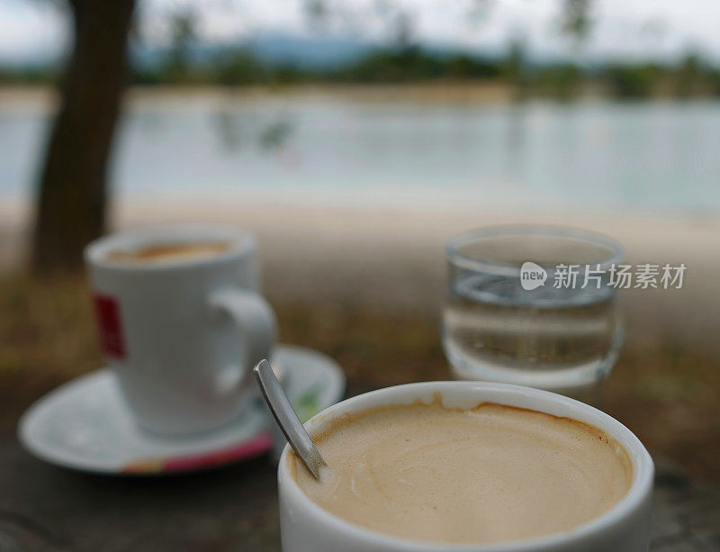 选择性对焦拍摄的一杯咖啡在一个湖岸边的餐厅的木桌