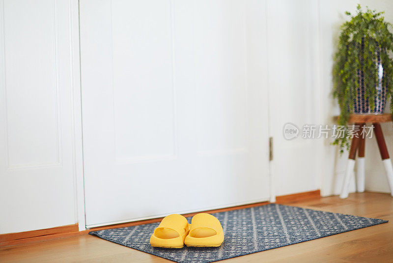 前门，门垫和黄色的室内凉鞋在明亮的现代家居环境。