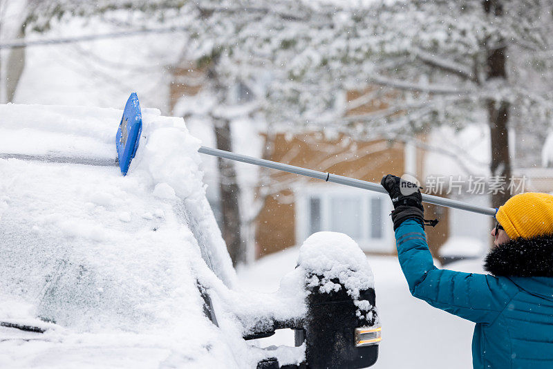 一名年轻女子在暴风雪后清理车上的积雪