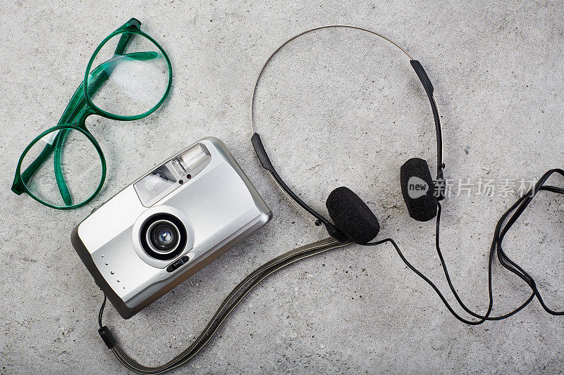 混凝土上的银色点拍胶片相机、眼镜和耳机。潮人的文化项目