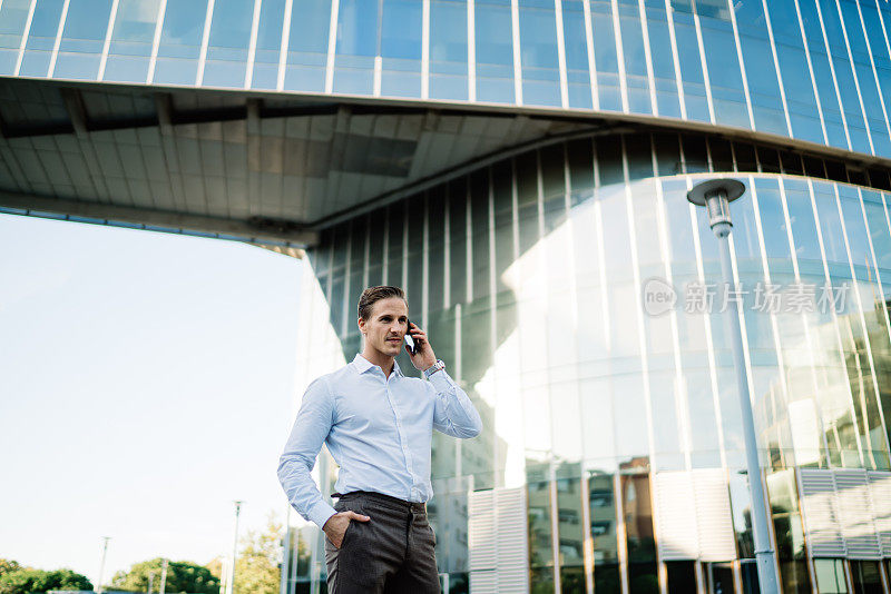 穿着白衬衫的英俊商人连接漫游，进行智能手机咨询对话，站在金融区的城市，自信的男性企业家通过手机应用程序打电话