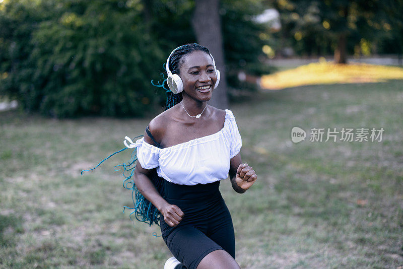 一名非洲年轻女子一边听着音乐，一边伸展身体，准备在大自然中进行训练。