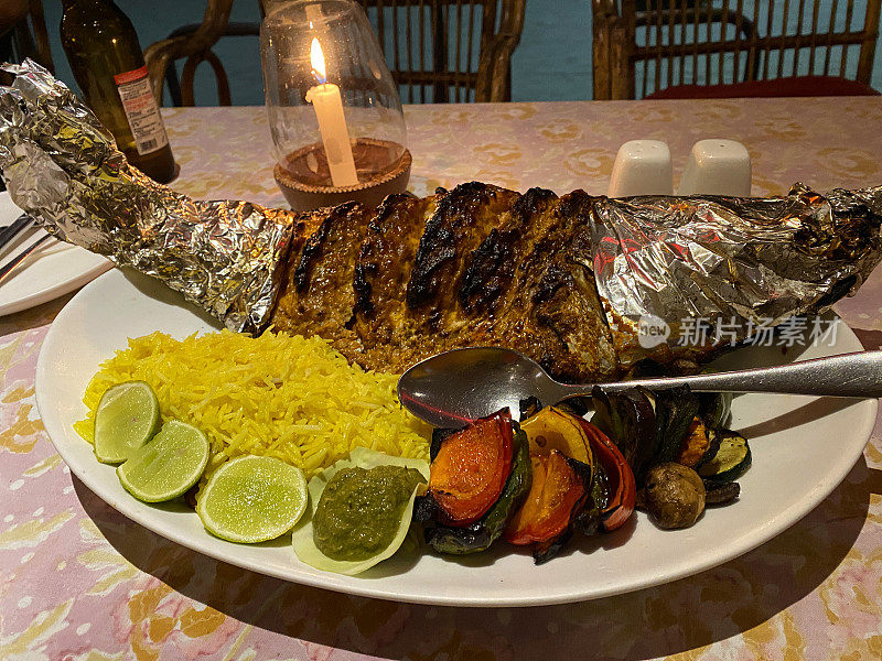 海滩餐厅场景的特写图像，土灶红鲷鱼餐，烤鱼配薯条，米饭和调味品在白色盘子上，鱼在铝箔，高架视图