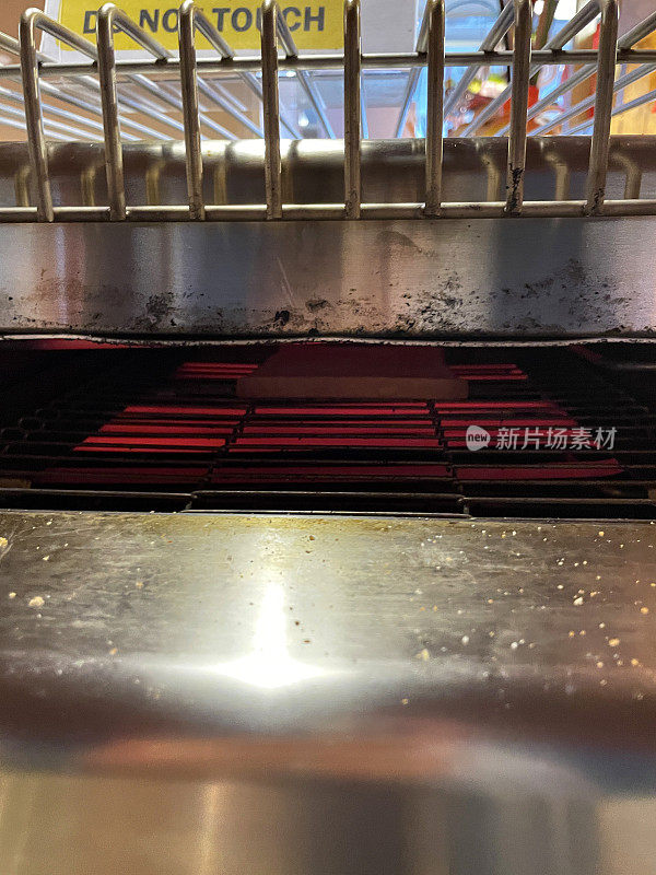 不锈钢商业传送带烤面包机烤架中红色发热元件的特写图像，重点放在前景