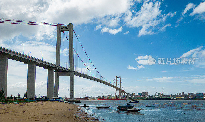 在莫桑比克马普托，以城市为背景的桥附近的海滩上的图像和港口码头的船只正在装载。