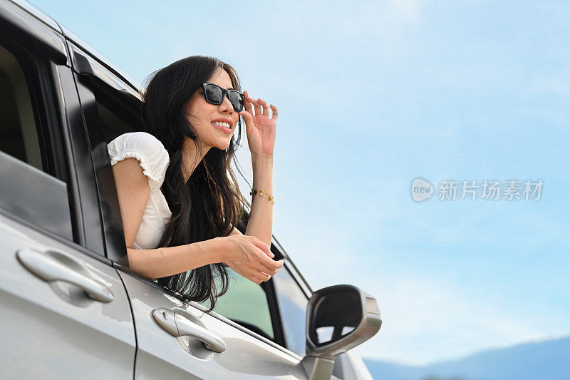 微笑的千禧一代女性穿着休闲时尚的衣服倚靠在车窗外，享受着夏日日落的景色