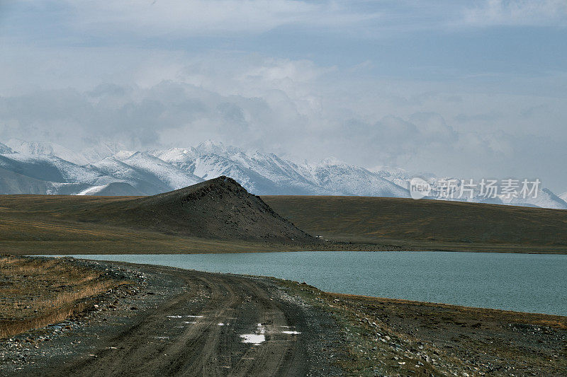 在秋天高原山谷的山湖边的道路，背景是白雪皑皑的山峰