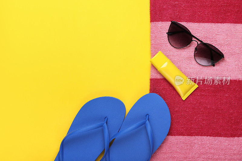 人字拖，防晒霜，时髦的太阳镜和黄色背景的条纹毛巾，平躺着。文本空间
