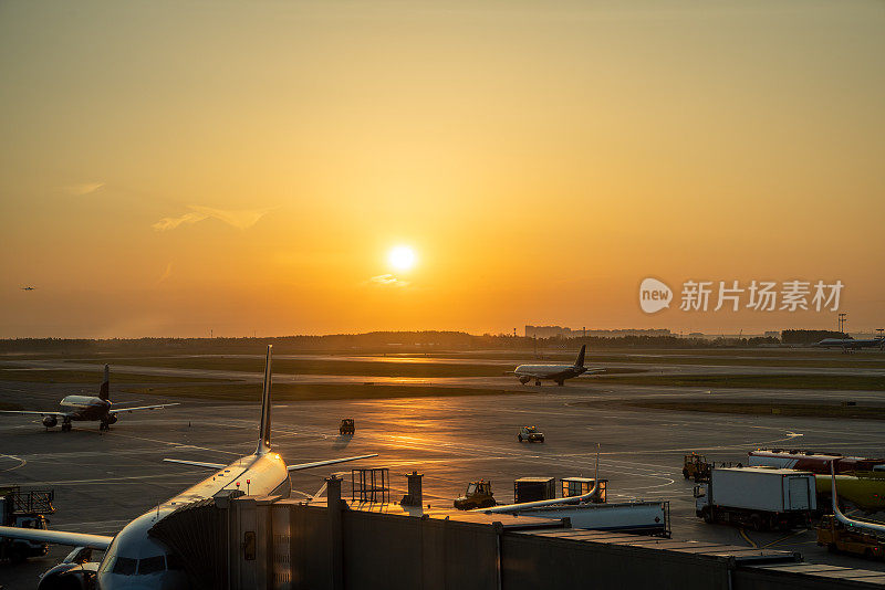 机场，在日落时停着客机。其中一架飞机停靠在旅客登机桥上