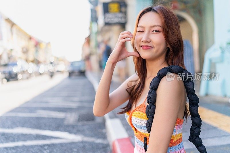 这位Z世代亚洲女性在普吉岛老城的路边摆出可爱的姿势，在她的旅行冒险中享受着放松的时刻